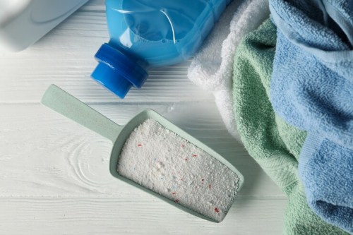 scoop-with-powder-detergent-towels-white-wooden-table_185193-26732